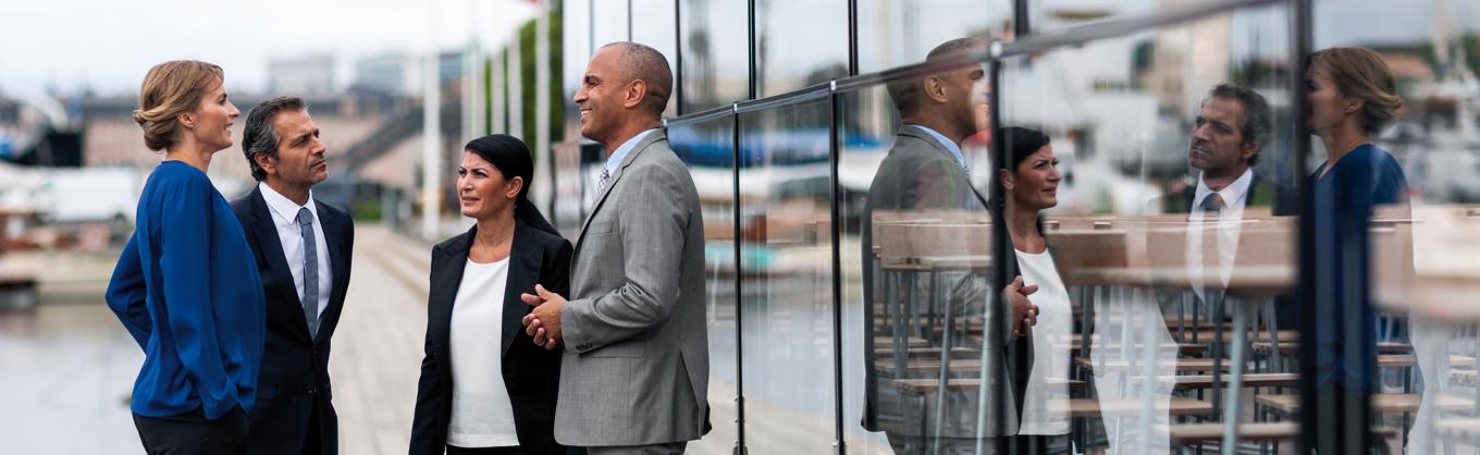 Business group with four people having a discussing outdoors in front of a glass wall.